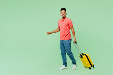 Sideways traveler man wears summer casual clothes hold bag suitcase walk go isolated on plain green background. Tourist travel abroad in free spare time rest getaway. Air flight trip journey concept.
