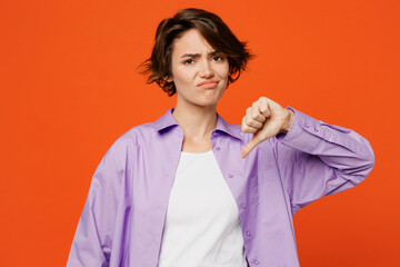 Young disatisfied upset sad caucasian woman she wear purple shirt white t-shirt casual clothes showing thumb down dislike gesture isolated on plain orange background studio portrait Lifestyle concept