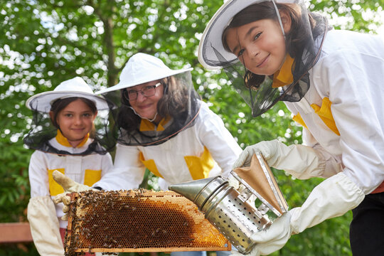 Smiling female beekeeper and girls holding honeycomb frame with smoker