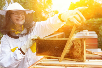 Female apiarist brushing off bees from hive frame with broom