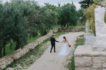 Happy stylish smiling couple walking in Tuscany, Italy on their wedding day. The bride and groom walk down the street by the hands. A stylish young couple walks. Husband and wife communicate nicely