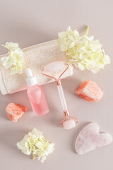 quartz roller massager, gua sha, matte bottle with a cosmetic product for maasage and face and body skin care. Vertical view. hydrangea flowers.