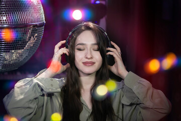 A beautiful girl in headphones enjoys music against the background of light rays from a disco ball. Disco, party.