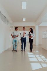 The director conducts a conversation with the secretary and a young programmer in a modern and spacious corridor of a large company, discussing various business topics and projects.