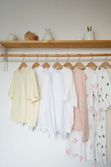 Child clothes on hangers in a room with white walls and wooden shelf in the interior