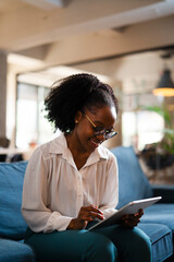 Beautiful African businesswoman sitting on sofa in office. Young woman using digital tablet.