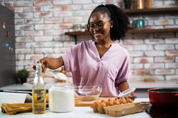 Fototapeta na wymiar Young African woman in kitchen. Beautiful woman having fun while making dough
