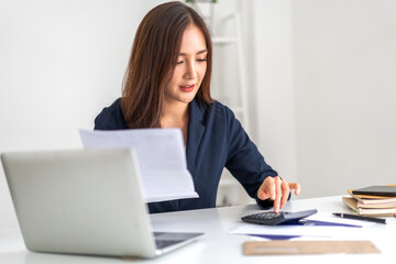 Smiling asian woman using calculator and calculate bills on laptop, paying bill, credit card, finance, tax, vat, credit card,  payment, tax refund, budget, debt, money.financial and accounting concept