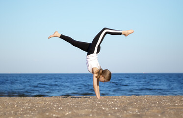 A young sporty girl  does somersaults with raised legs against the background of the sea. Selective focus. Blurred background