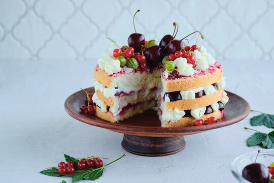 Summer cake with custard, raspberry jam and assorted berries on a clay plate on a light concrete background.
