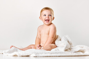 Cute, adorable baby, child in calmly sitting in towel and smilling against white studio background. After shower. Concept of childhood, newborn lifestyle, happiness, care. Copy space for ad - obrazy, fototapety, plakaty