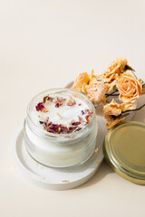 Handmade candle from paraffin and soy wax in glass with wooden wick and dry herbal isolated on pastel beige background. Flat lay, top view, copy space