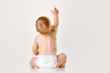 Back view image of little baby, child, toddler sitting in diaper against white studio background....