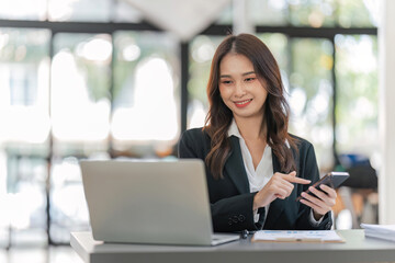 Young business woman on the phone at office. Business woman texting on the phone and working on laptop. Pretty young business woman sitting on workplace