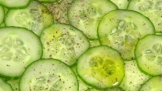 Top view fresh cucumber slices with black pepper and olive oil rotate. Background of chopped cucumber slices for cooking show, restaurant, cafe, fast food. Moisturizing skin and smoothing wrinkles