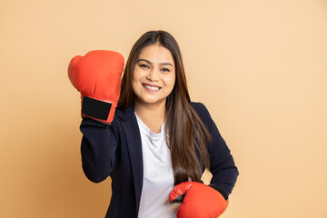 Happy young indian woman employee wearing boxing gloves punching isolated over beige background.