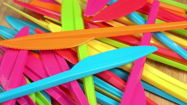 Pile of colorful plastic knives on cutting board surface. Plastic disposable tableware rotating. Disposable tableware for kitchen, restaurant, delivery, picnic