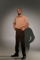 real people, bold african american man with myasthenia gravis standing with hands in pockets on grey background, dark skinned person in shirt, smart casual, diversity and inclusion, ptosis