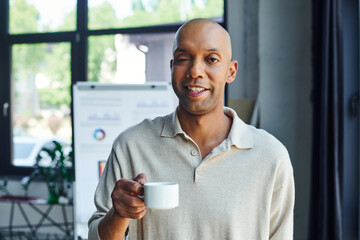chronic illness, inclusion, bold african american man with myasthenia gravis disease holding cup of coffee, happy and dark skinned office worker with ptosis syndrome looking at camera