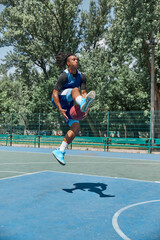 Slam dunk. Full-length image of young man in motion, playing basketball outdoors on sportsground on...