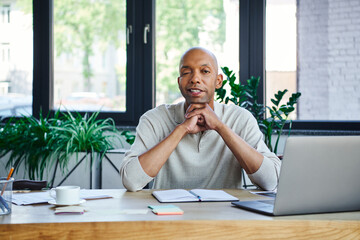 ptosis syndrome, bold african american businessman with eye syndrome looking at camera near laptop...