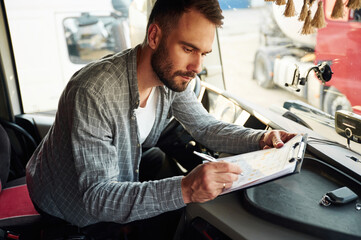Writing in the document, sitting inside. Young truck driver in casual clothes