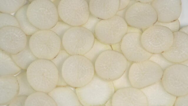 Sliced daikon radish rotates on a plate as a background. Mooli or Daikon, Raphanus sativus, displayed on a market stall, traditional japanese dish