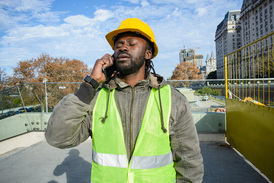 young black man construction worker with closed eyes is upset and tired talking on the phone