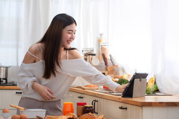 Happy pretty woman learning online cooking class via tablet computer in kitchen at home