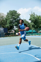 Dynamic image of young man, basketball player in blue uniform, training outdoors on playground on...