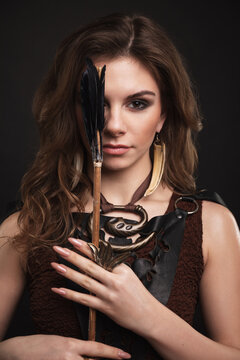 Fantasy fashion warrior woman with an arrow looking at the camera. Medieval archer female studio photography on the black background. 