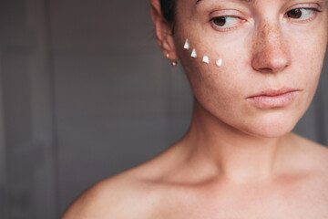 Woman with dots of cream on her face looking aside 