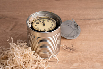 A tin can with an old clock is on the table. Removed lid and packaging material. Time management. Leeway. Background. Concept.
