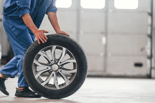 Walking with new tire. Auto mechanic working in garage. Repair service