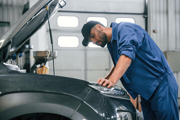 Naklejka premium Hood is opened. Auto mechanic working in garage. Repair service