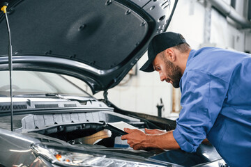 With tablet in hands. Auto mechanic working in garage. Repair service - obrazy, fototapety, plakaty