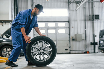 Fototapeta na wymiar New tire, moving it. Auto mechanic working in garage. Repair service