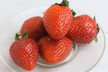 fresh ripe strawberries in a simple glass plate on a wooden table. Close-up