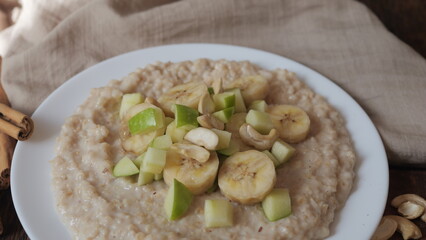 Plate of oatmeal porridge with green apple, cashew and banana. Close up.