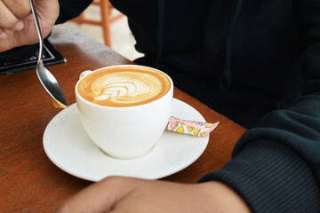 Man hand in blue sweater holding cup of cappuccino on the table. cup of coffee