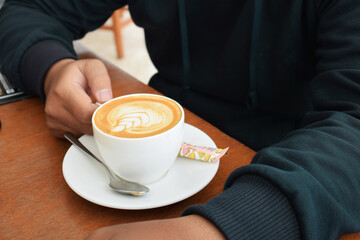 Man hand in blue sweater holding cup of cappuccino on the table. cup of coffee