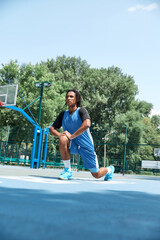 Young man, guy with dreads in uniform stretching before game, basketball training outdoors. Warm...