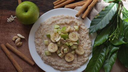 Plate of oatmeal porridge with green apple, cashew and banana. Close up.