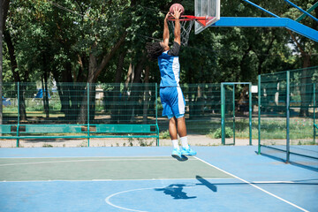 Full-length image of young man, sportsman playing basketball on warm sunny day. Outdoor...