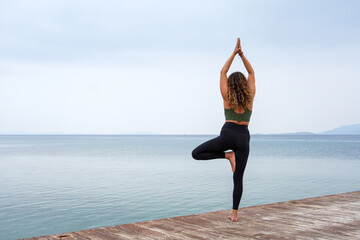 Woman practicing yoga by the sea on a deck - Vrksasana - Tree pose