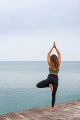 Woman practicing yoga by the sea on a deck - Vrksasana - Tree pose