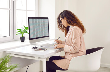 Focused businesswoman analyzing financial spreadsheet report on computer screen. Accountant, analyst, financial manager checking electronic spreadsheet and doing paperwork on office