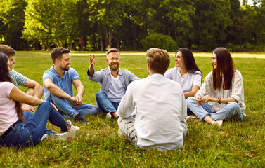 Friendship and communication. Group of young people communicate sitting on grass in park on summer...