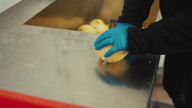 Closeup shot of skilled professional slicing raw peeled celery roots on steel counter and placing them in big red box. Hands carefully operating a kitchen knife. High quality 4k footage