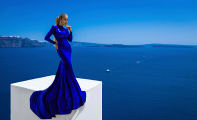 Elegant woman in blue long sequin dress is posing outdoor in luxury resort in Santorini. Female...